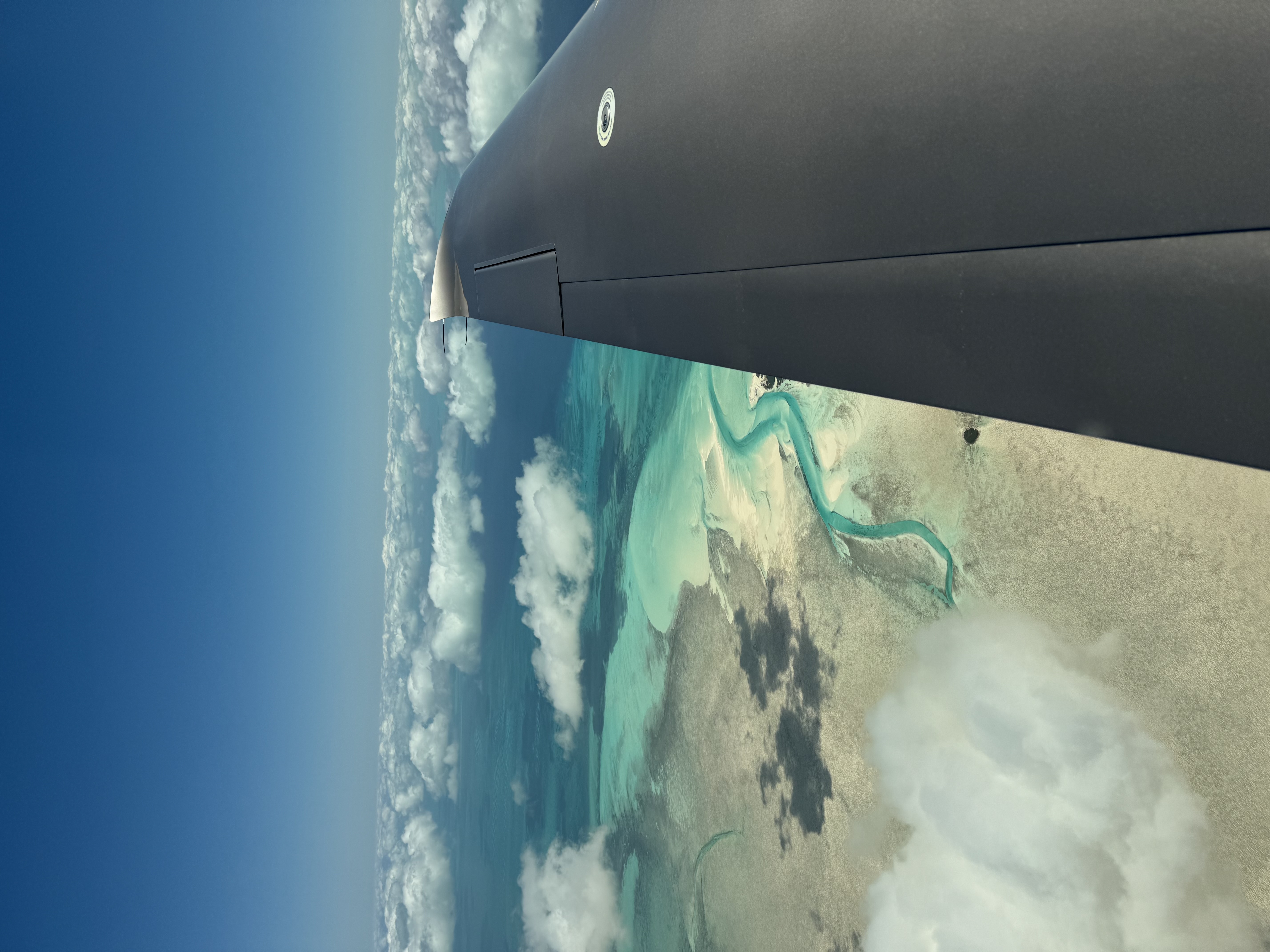Aerial view from the wingtip over turquoise sandbars and a winding tidal channel